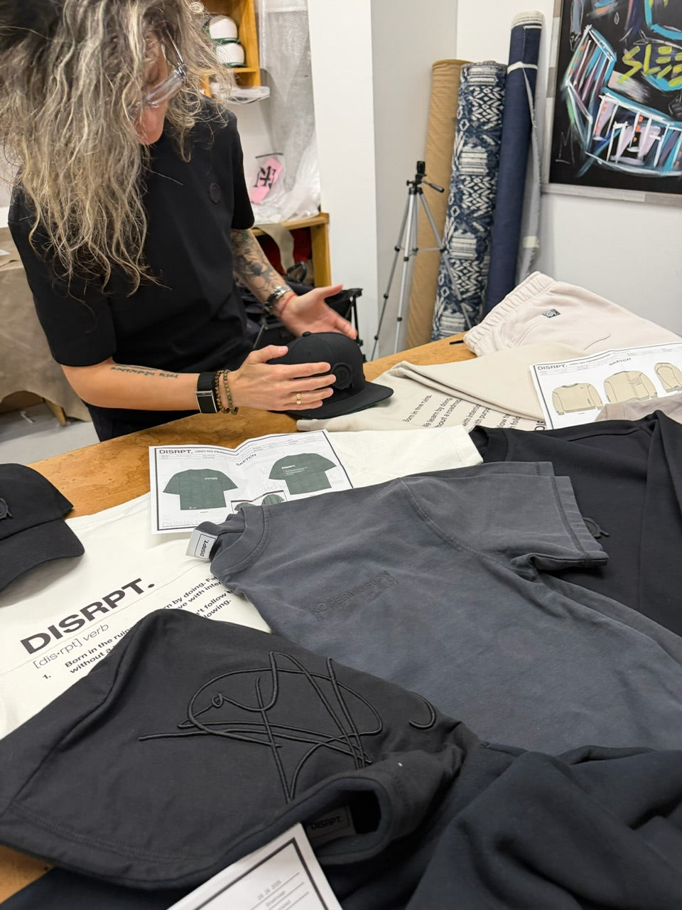 DISRPT behind the scenes design process with clothing samples, sketches, and materials on studio workspace