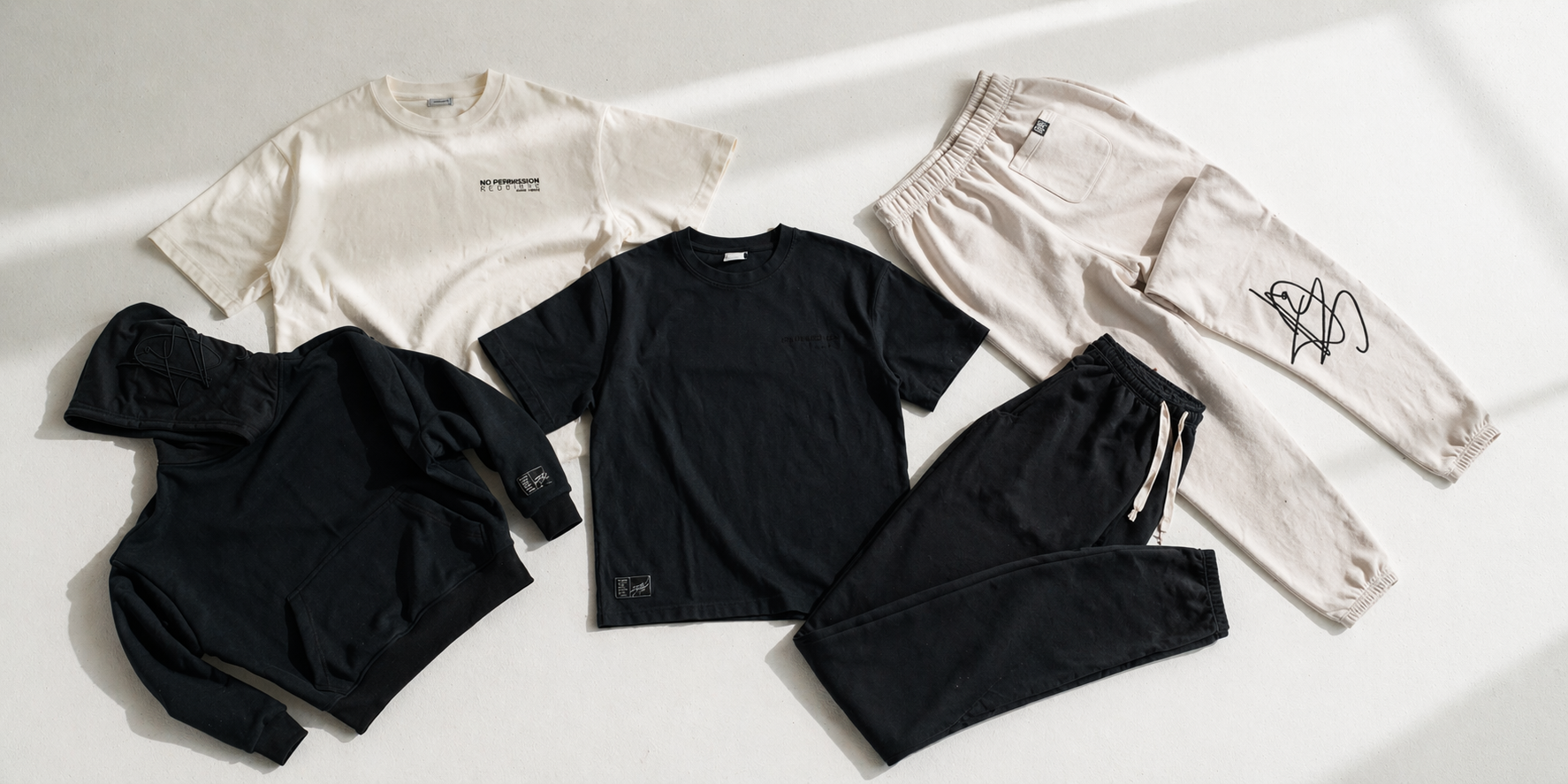 Flat lay of DISRPT collection featuring black and bone hoodie, t-shirts, and sweatpants styled together on a minimal background
