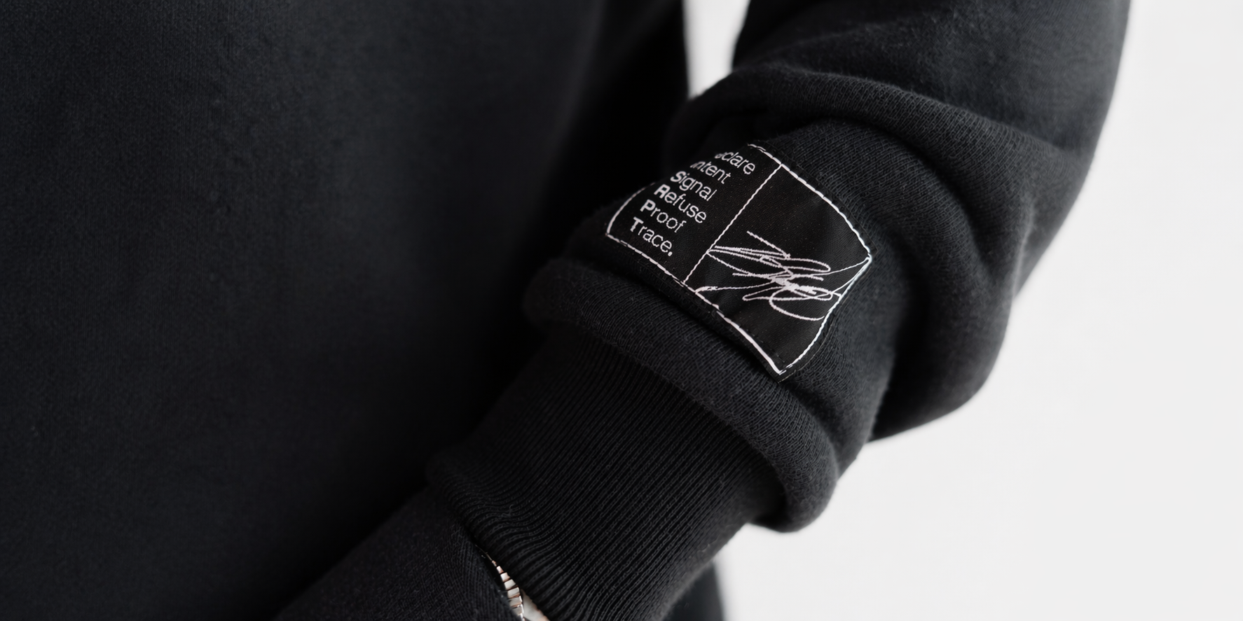 Close-up of DISRPT black hoodie sleeve showing signature label patch stitching and premium fabric detail
