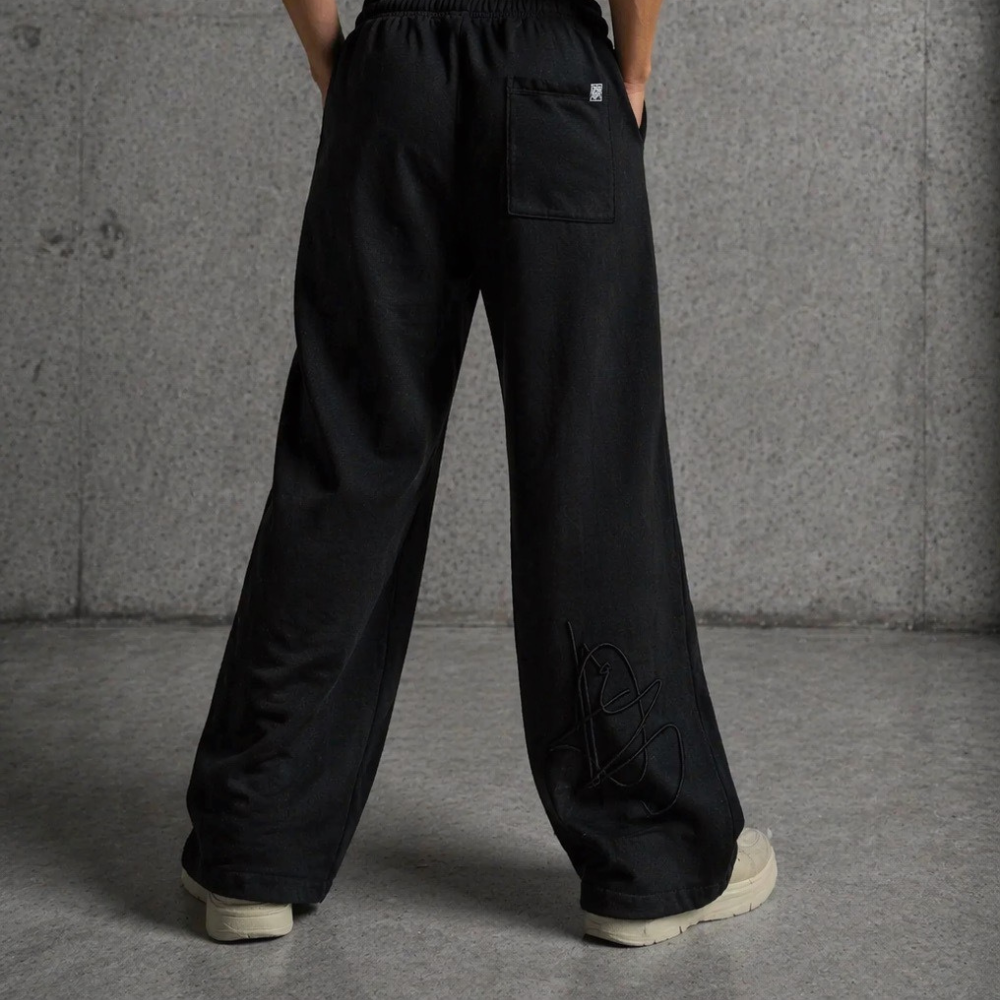 Back view of DISRPT black signature sweatpants showing relaxed fit, wide leg silhouette, back pocket, and logo detail