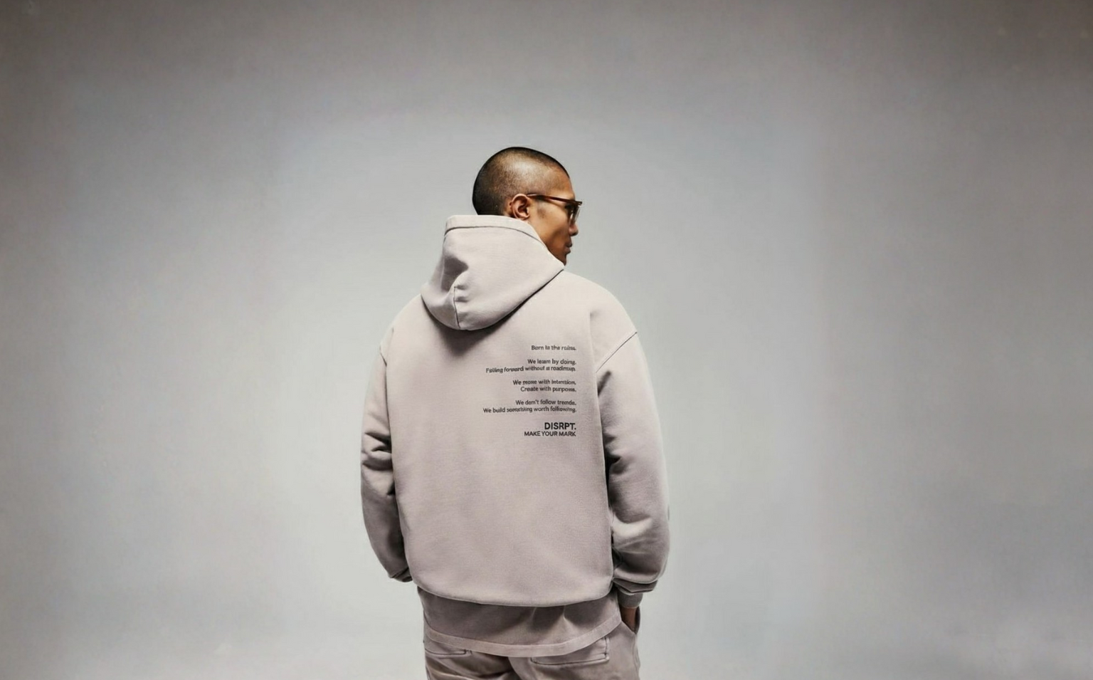 Person wearing gray DISRPT hoodie and sweatpants back view on plain background with logo text and minimalist design